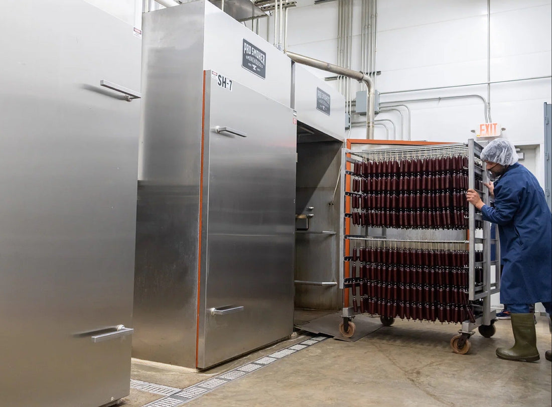Worker loading Multi-truck commercial Pro Smoker with rack of smoked snack sticks